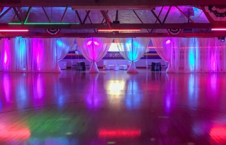 An empty roller skating rink illuminated with pink and blue lights, with white drapes and a shiny floor.