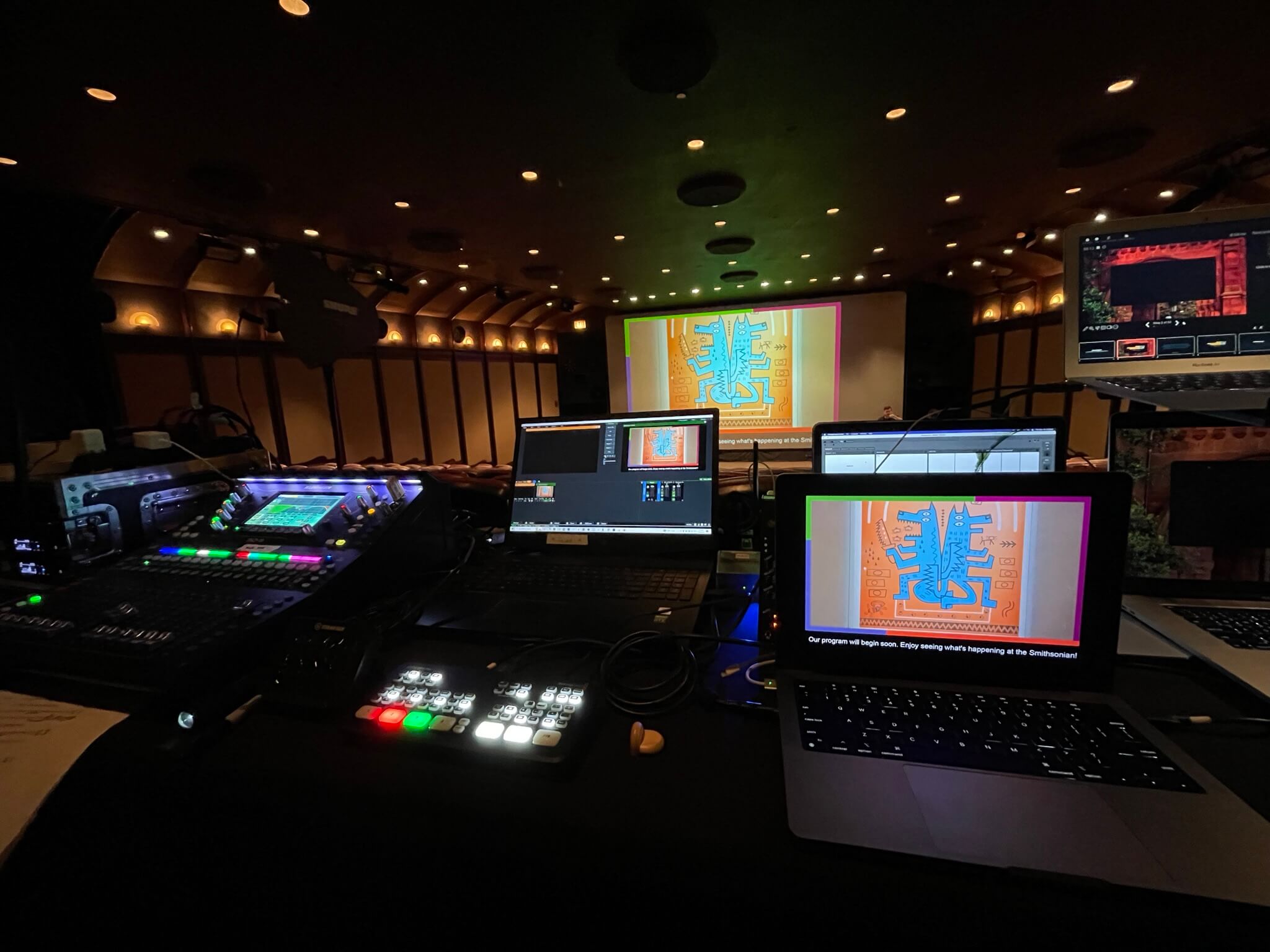 Control room with multiple monitors and lighting equipment during a live performance.