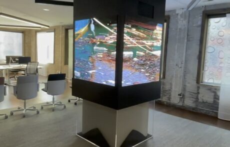 A modern office space with a large, pillar-like digital display screen showing colorful graphics.