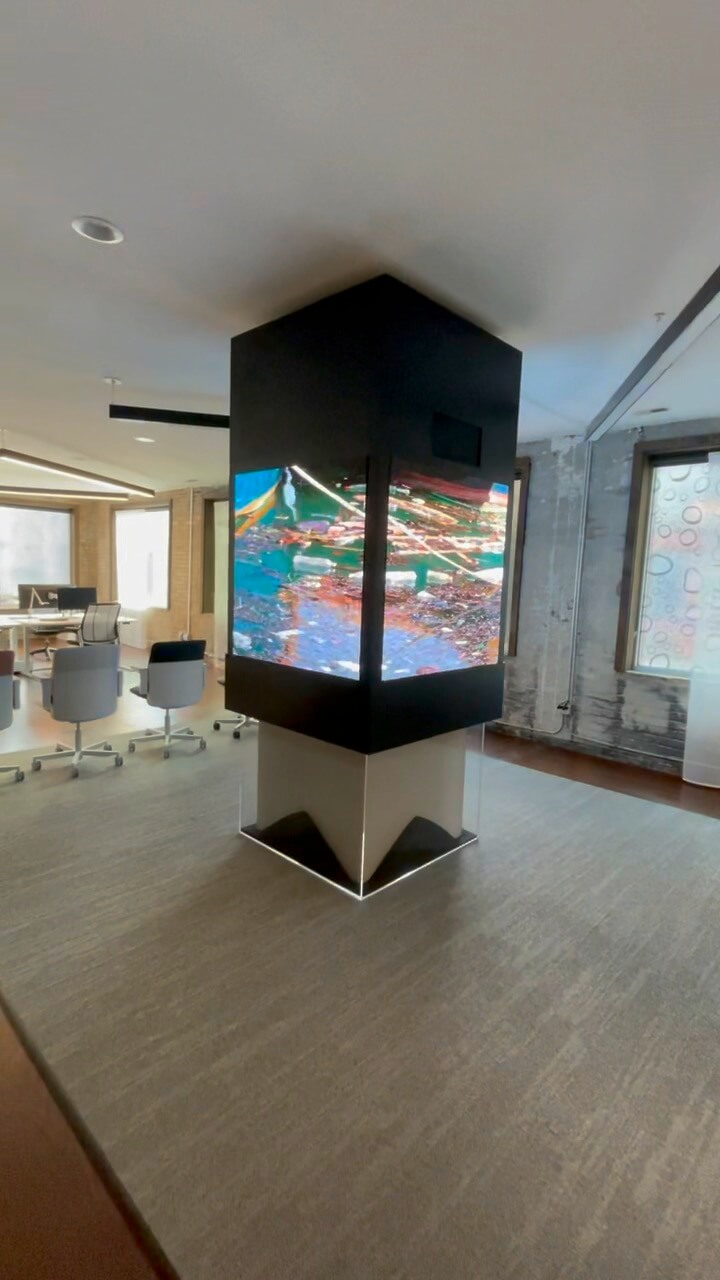 A modern office space with a large, pillar-like digital display screen showing colorful graphics.