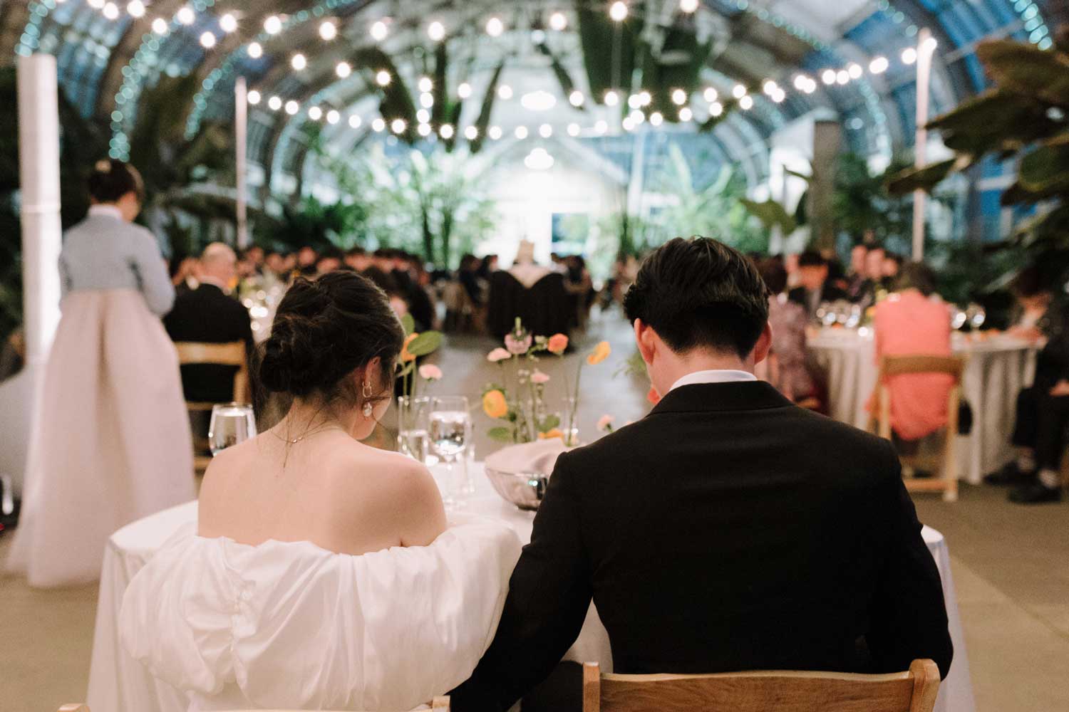 A couple seated at a wedding reception in a glasshouse venue.