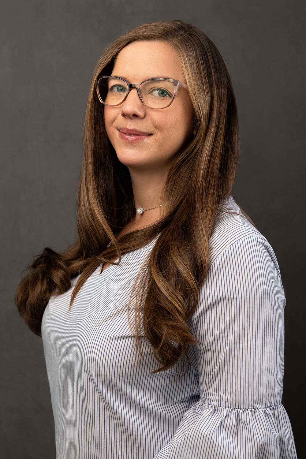 Professional woman with glasses posing for a portrait against a gray background.