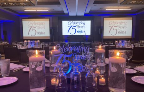 A banquet hall set up for a celebration with tables, candles, and a screen displaying "celebrating 75 years.