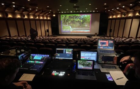 A view from a control booth at the back of a theater with technicians operating equipment during a screening.