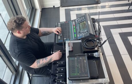 A man adjusting equipment on a sound mixing board at an indoor venue.