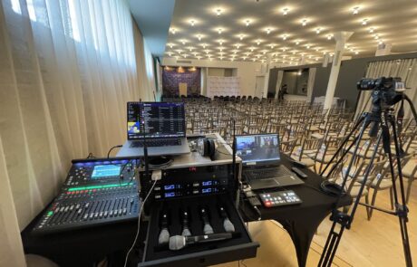 Audio-visual control station set up at the rear of a conference room with empty chairs and presentation equipment.
