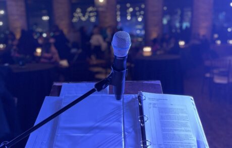 Microphone and sheet music on a stand with a blurred audience in the background, suggesting a live music performance setting.