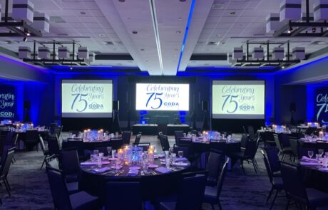 Banquet hall set up for a celebration event with tables, centerpieces, and a stage displaying "celebrating 75 years" signage.