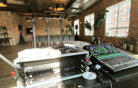 Sound mixing equipment set up in a room with exposed brick walls and hanging golden lights, ready for an event.