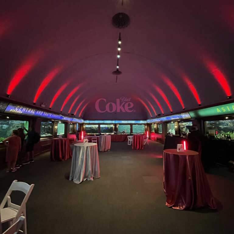 Event venue with red ambient lighting and round tables draped with cloths.