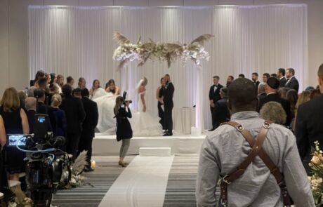 A wedding ceremony in progress with guests and a photographer in the foreground, and the couple standing at the altar.