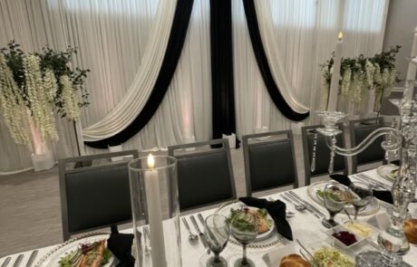 An elegantly set dining table at an event with white and black drapery in the background.