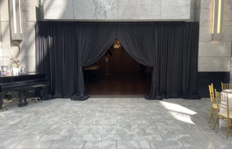 An empty event space with a piano to the side, black curtains across the back, and chairs around the perimeter.