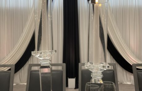 Symmetrical table setting for a formal event with tall glass candlesticks, fine dinnerware, and elegant drapery.