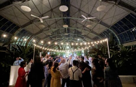 People dancing at an evening event in a venue with a curved, glass ceiling.