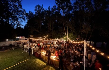 An outdoor evening event with guests seated at tables under string lights.