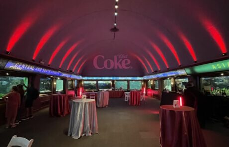 Dimly lit event space with circular tables dressed in red cloths, ambient red lighting, and aquarium views on the sides.