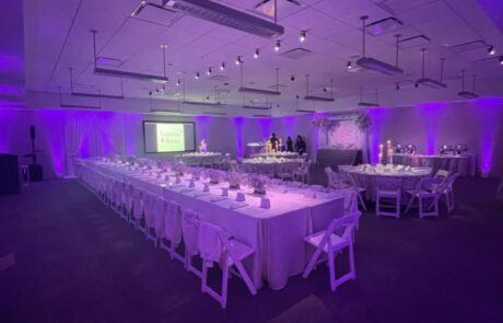 An event hall set up for a banquet with purple lighting and tables dressed in white linens.