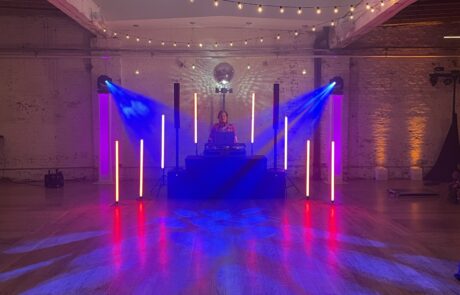 Dj performing at an indoor event with colorful lighting and a disco ball.