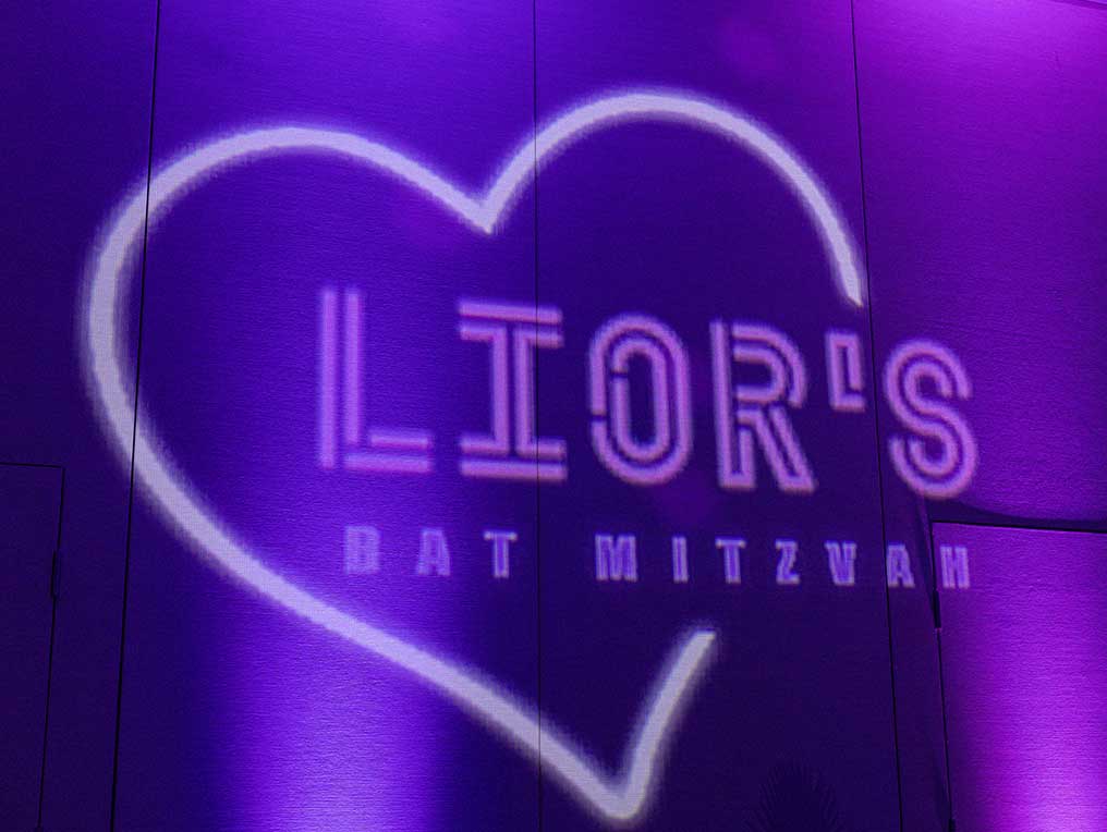 Purple lighting with a heart shape and the text "lior's bat mitzvah" projected onto a wall.