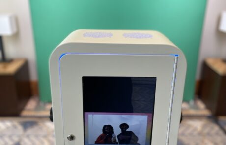 A digital kiosk with a touchscreen display reflecting two people's silhouette in a room with a green backdrop.
