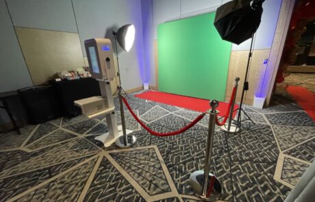 Photography or video recording setup with a green screen, lighting equipment, and a stanchion barrier in an indoor space.