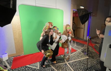 Group of people posing with fun props in front of a green screen at a photo booth setup.