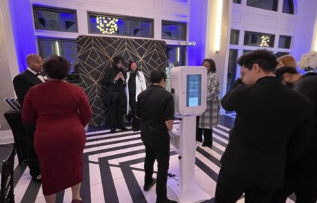 Guests queue at a check-in kiosk at an indoor event with a black and white checkered floor and modern decor.