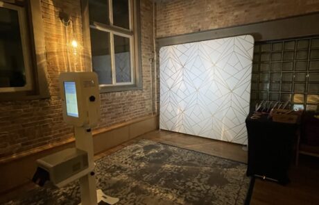 An empty photo booth set up in a room with exposed brick walls and industrial ceiling pipes.