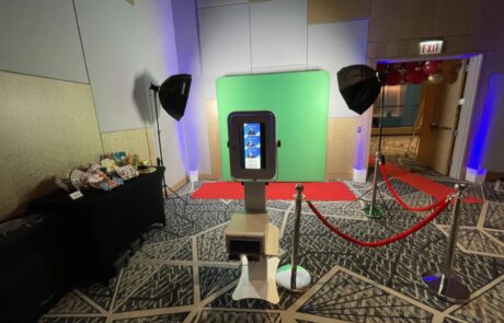 A photo booth set up with a red carpet and stanchions, flanked by two umbrella lights, with snacks arranged on a table to the side.