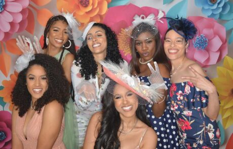 A group of women smiling and posing at a party with a colorful floral backdrop.