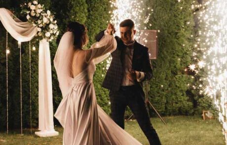 A bride and groom dance outdoors at night with sparklers in the background, creating a festive atmosphere.