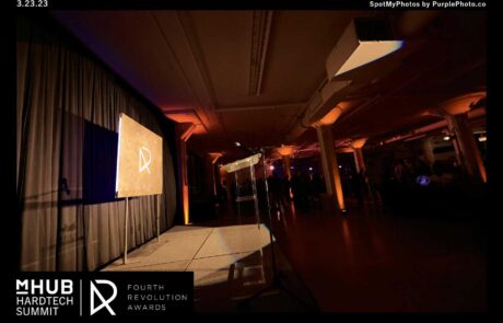 A dimly lit event space with a screen displaying a logo, associated with the mhub hardtech summit and fourth revolution awards.