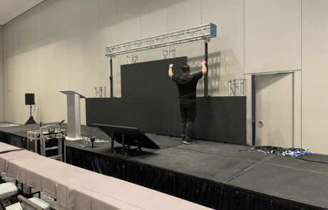A person setting up equipment on a stage in a conference room.